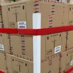A red StrapPRO reusable strap by Lynksols securing a pallet loaded with boxes and the Edge Protector product protecting the 4 corners of the load.